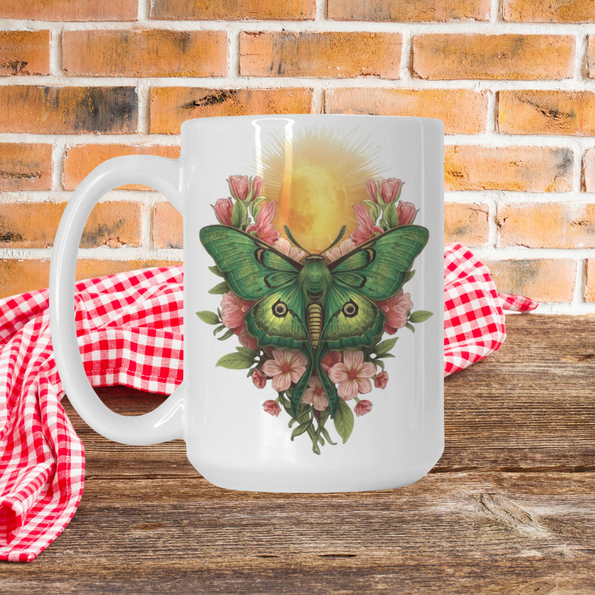 White mug with a green lunar moth and floral design on a wooden picnic table with a brick wall background.