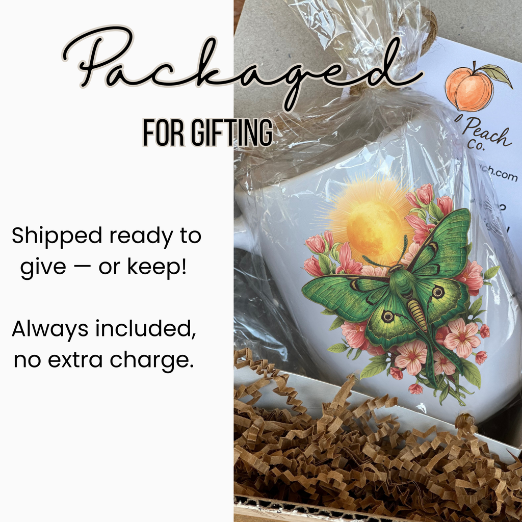 White mug in gift packaging with a design of a lunar moth and flowers, labeled 'Artful Peach Co'.