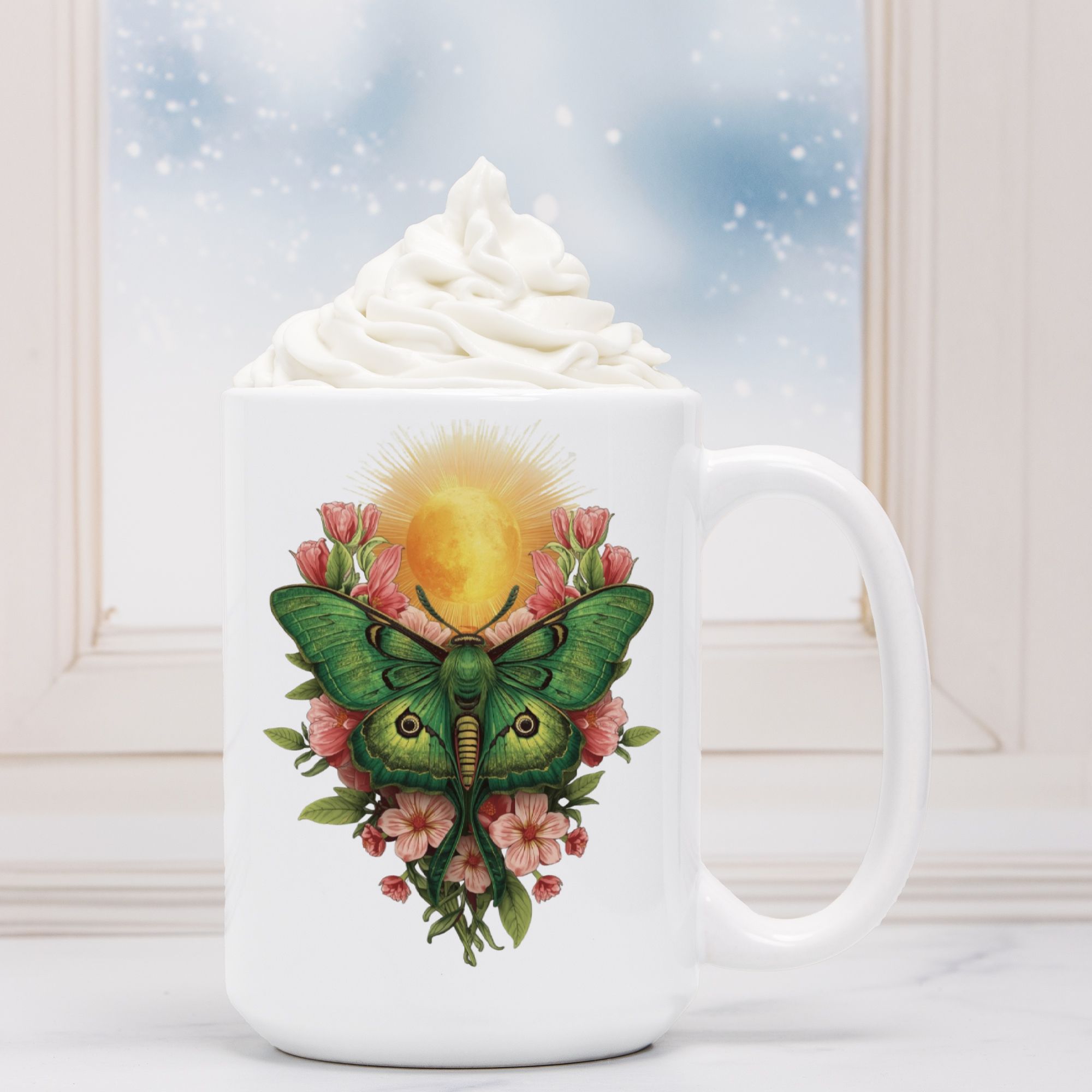 White mug with a green lunar moth and floral design, filled with hot chocolate and whipped cream.