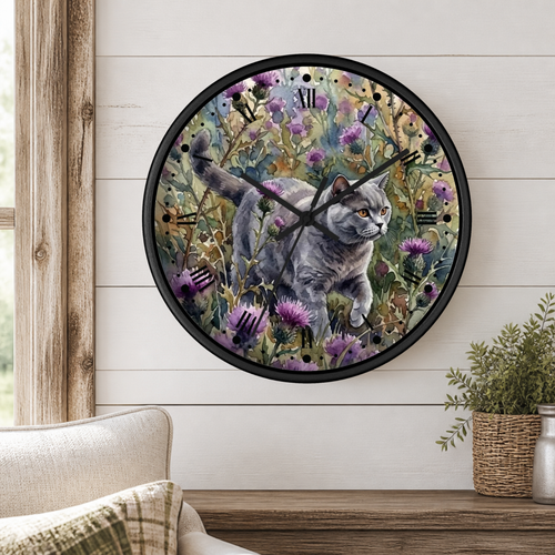 A round wall clock with a black frame and a printed illustration of a gray cat walking through purple flowers, mounted on a white shiplap wall above a wooden table with a plant and part of a sofa visible.