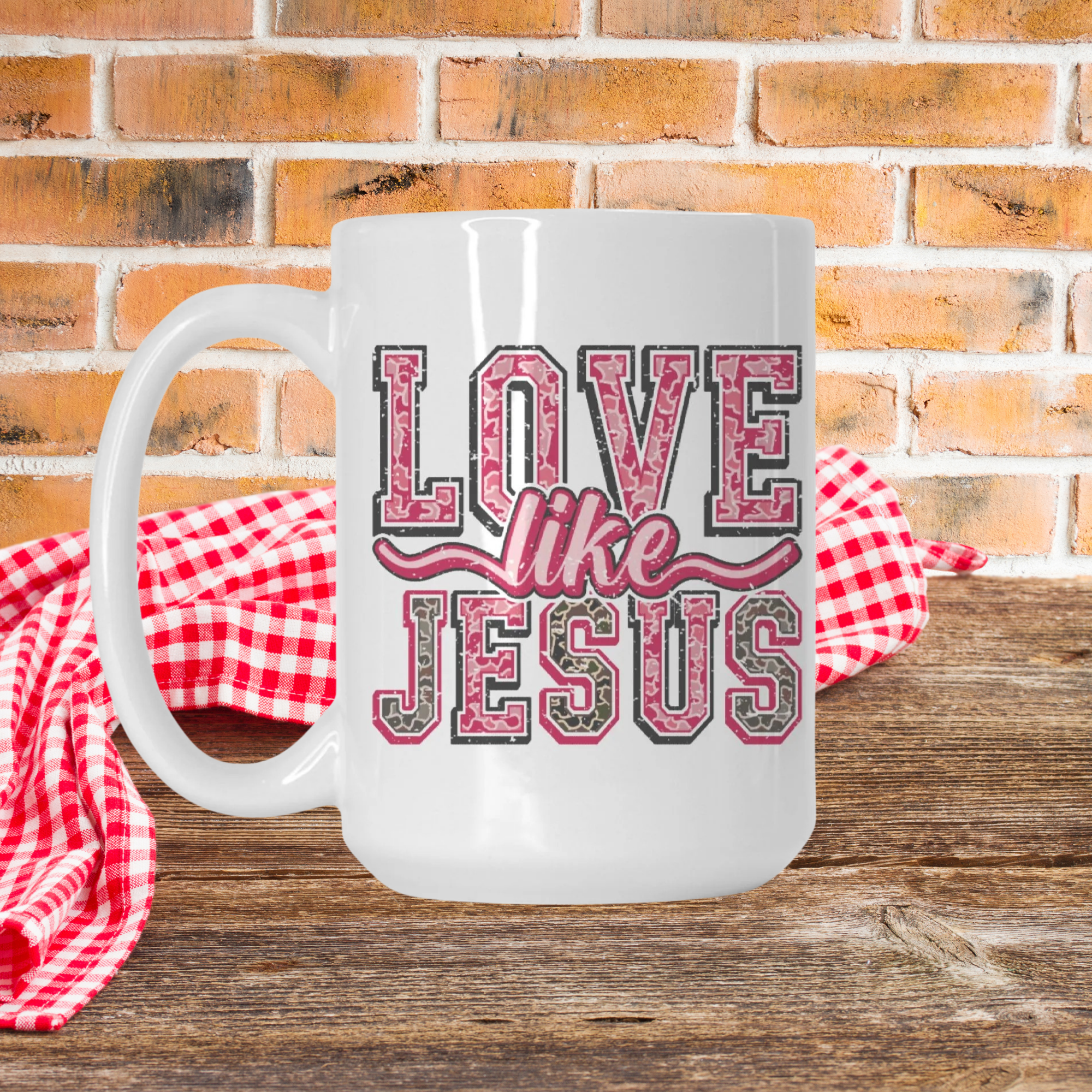 White mug with the design pink and grey text 'Love Like Jesus' on a wooden picnic table and brick wall background.