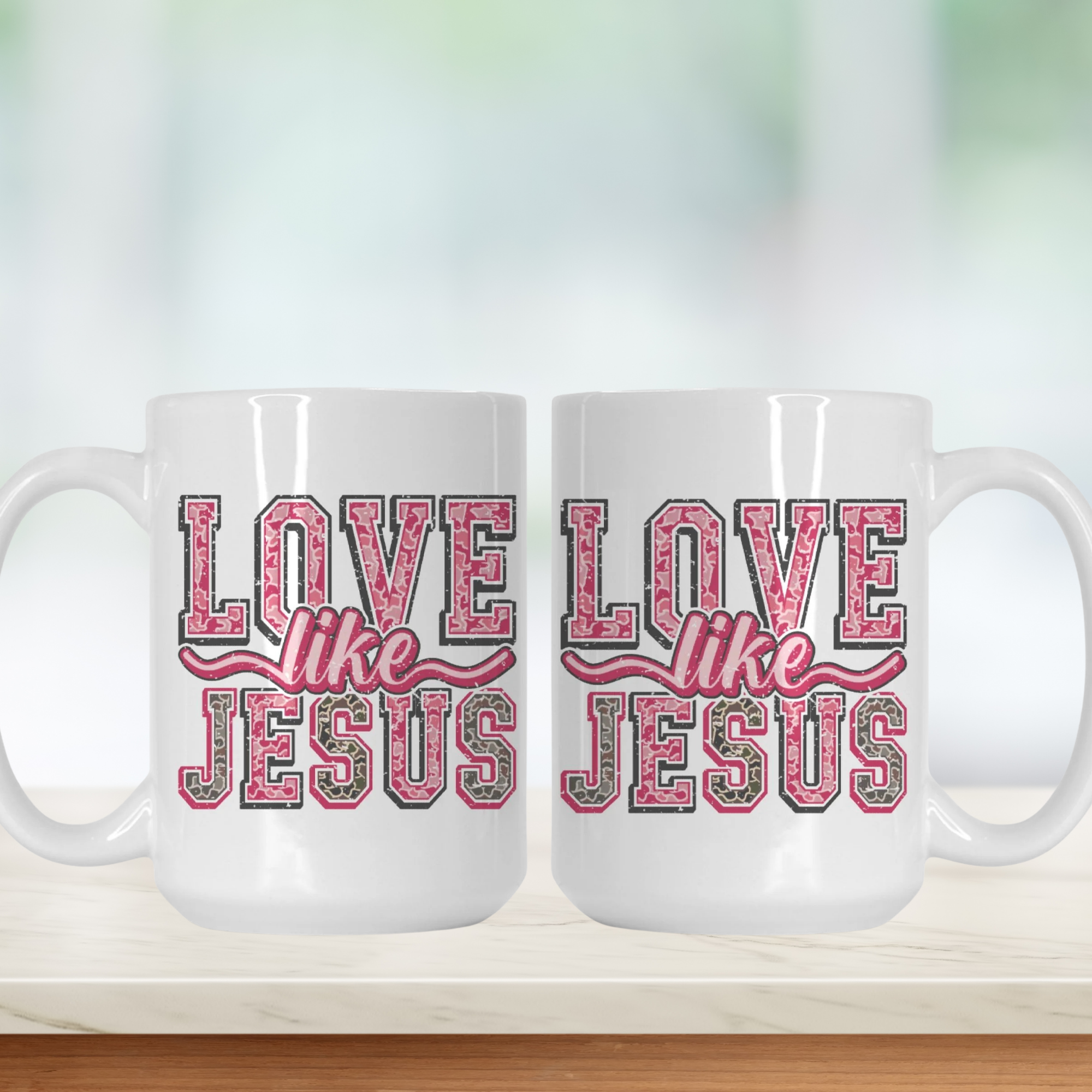 Two white mugs with 'Love like Jesus' text in pink and grey on a blurred background