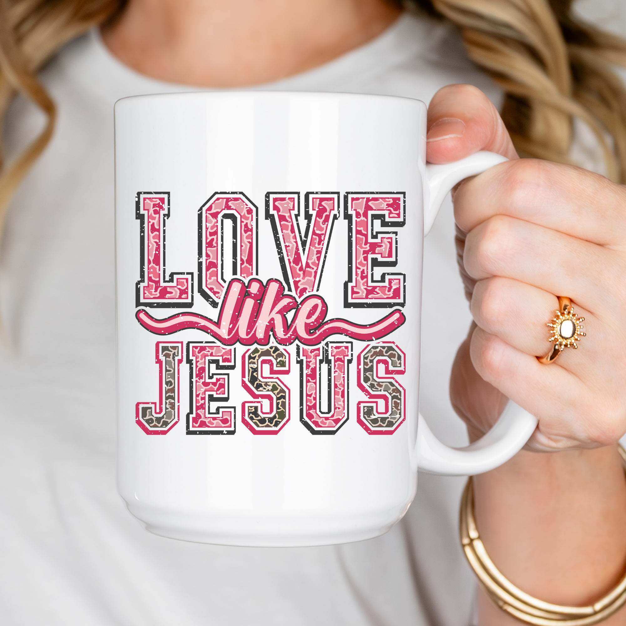 White mug with 'Love like Jesus' text held by a person wearing a white shirt.