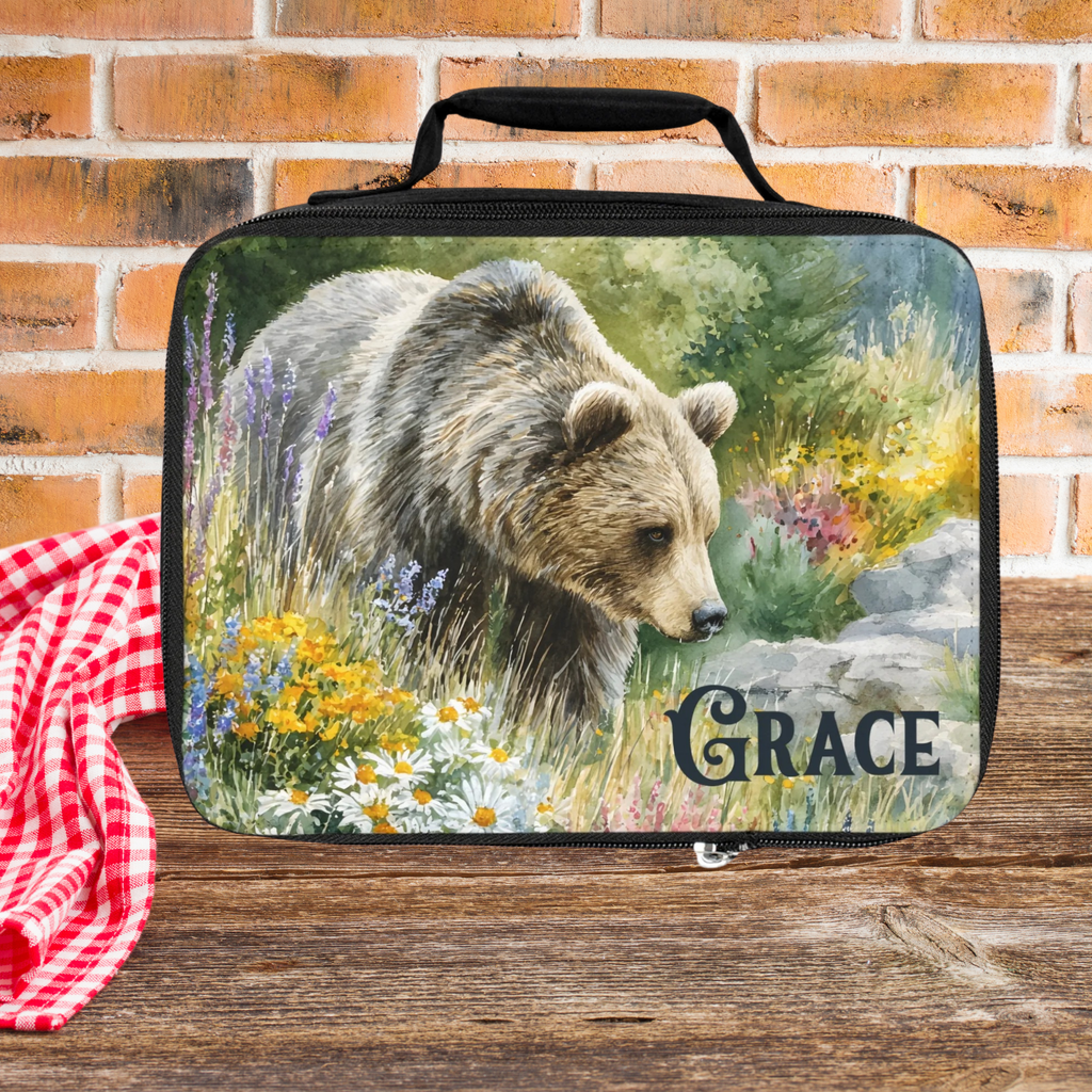 Lunch bag with bear design and 'Grace' custom text on a picnic table against a brick wall background