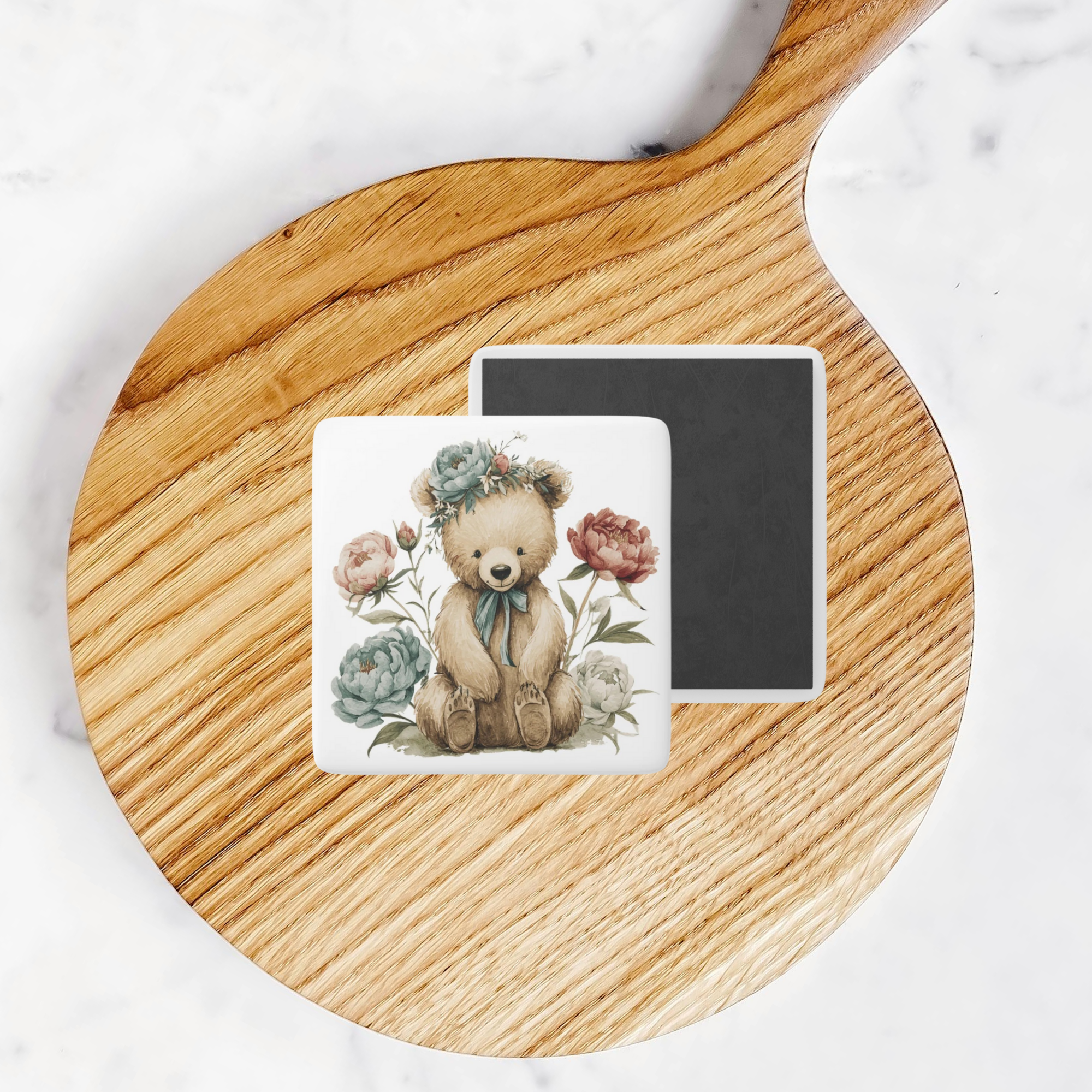 Two square magnets with teddy bear and floral designs on a wooden board.