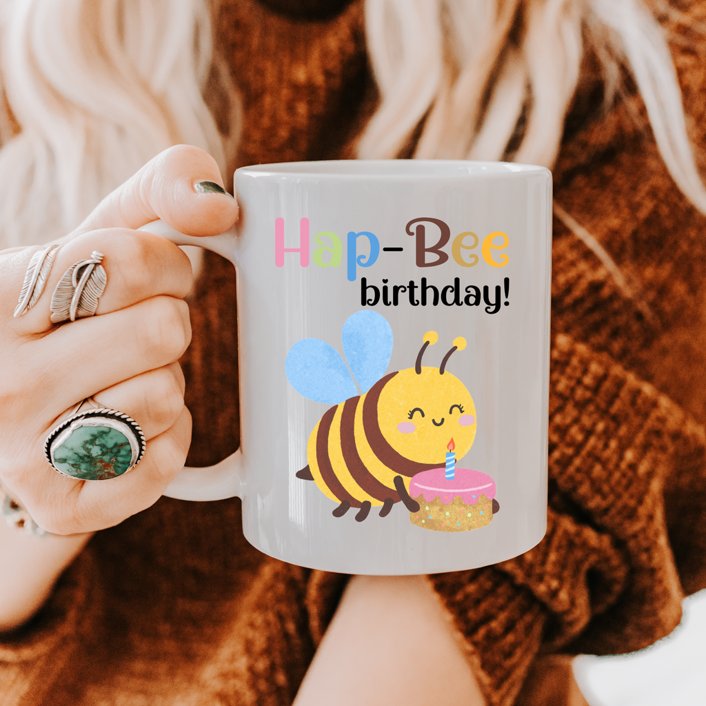 Person holding a mug with a bee design and 'Hap-Bee birthday!' text.