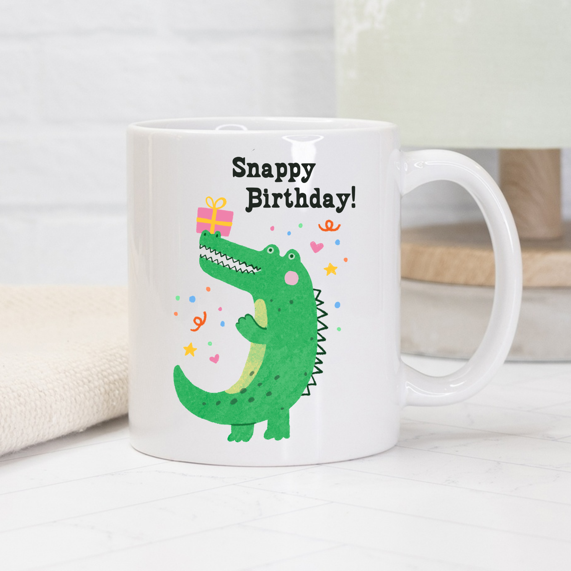 White mug with a green dinosaur illustration and 'Snappy Birthday!' text on a white background