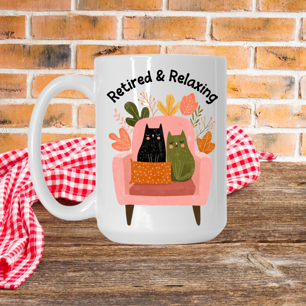 White 15oz. mug with a design of two cats on a chair and text 'Retired & Relaxing' against a brick wall background.