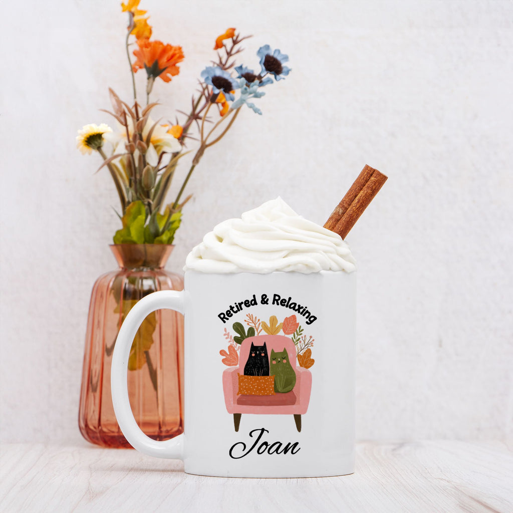 Mug with 'Retired & Relaxing' design featuring cats sitting in a chair, cinnamon stick, and flowers in the background.