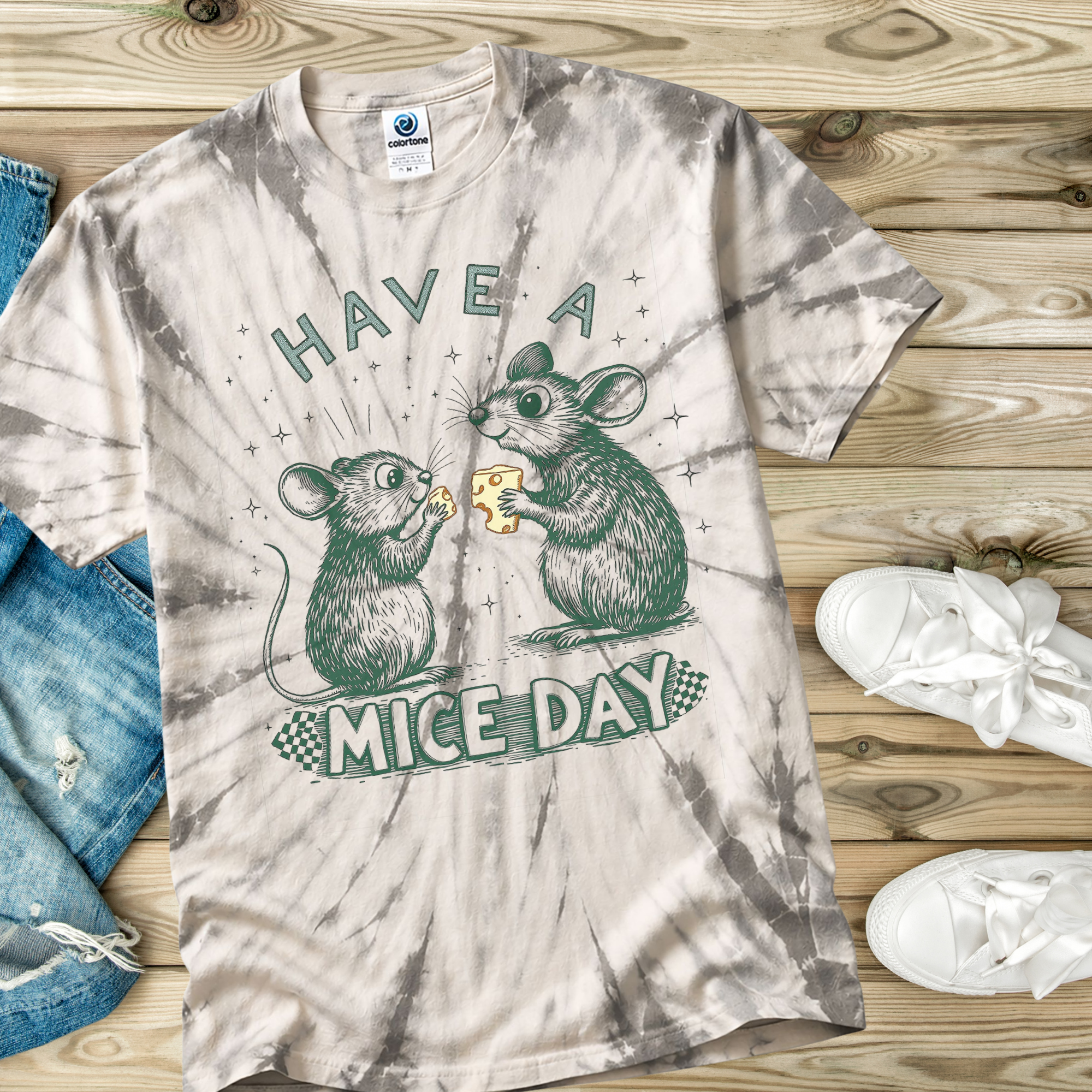 Tie-dye t-shirt with mouse design and text 'Have a Mice Day' on a wooden surface.