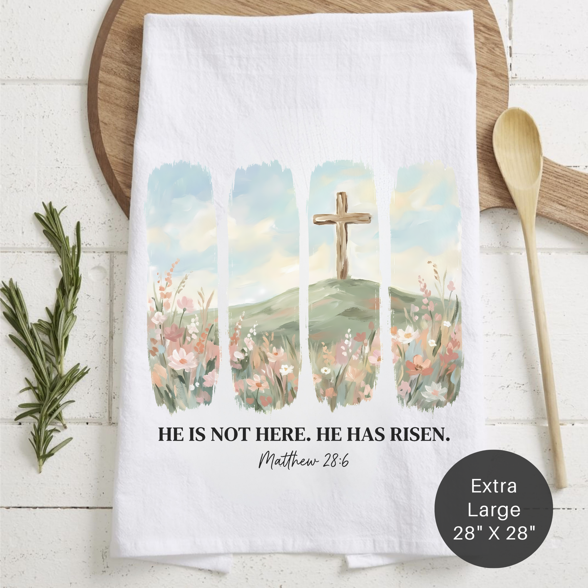 Tea towel with cross and flower design, featuring 'He is not here, He has risen' text, on a wooden surface.