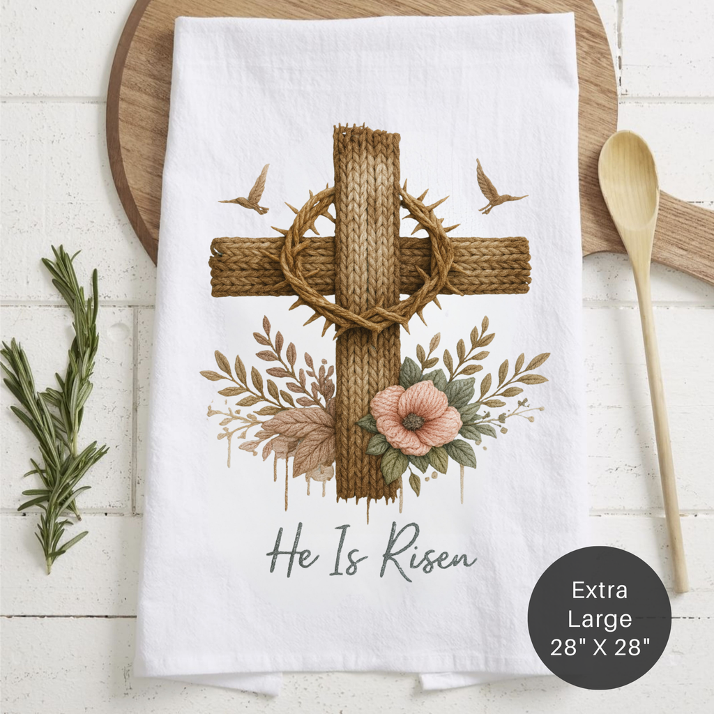 White towel with a cross and floral design, featuring the text 'He Is Risen' on a wooden surface.