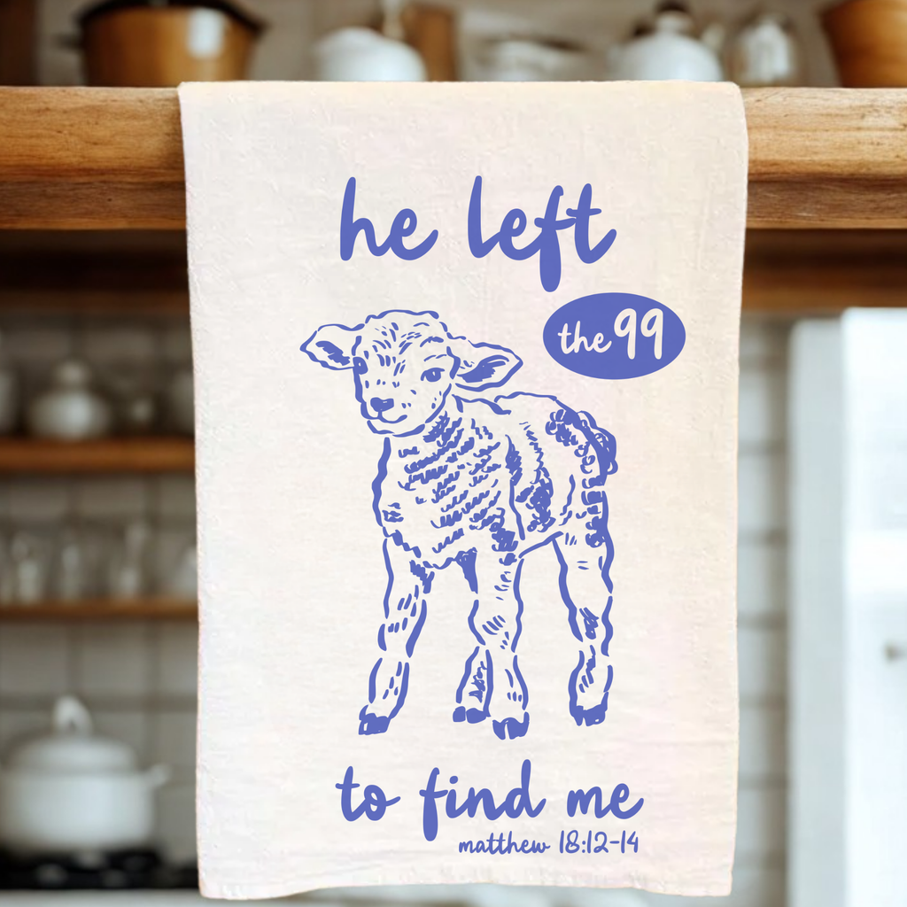 Kitchen tea towel with blue sheep illustration and text on a wooden rack.