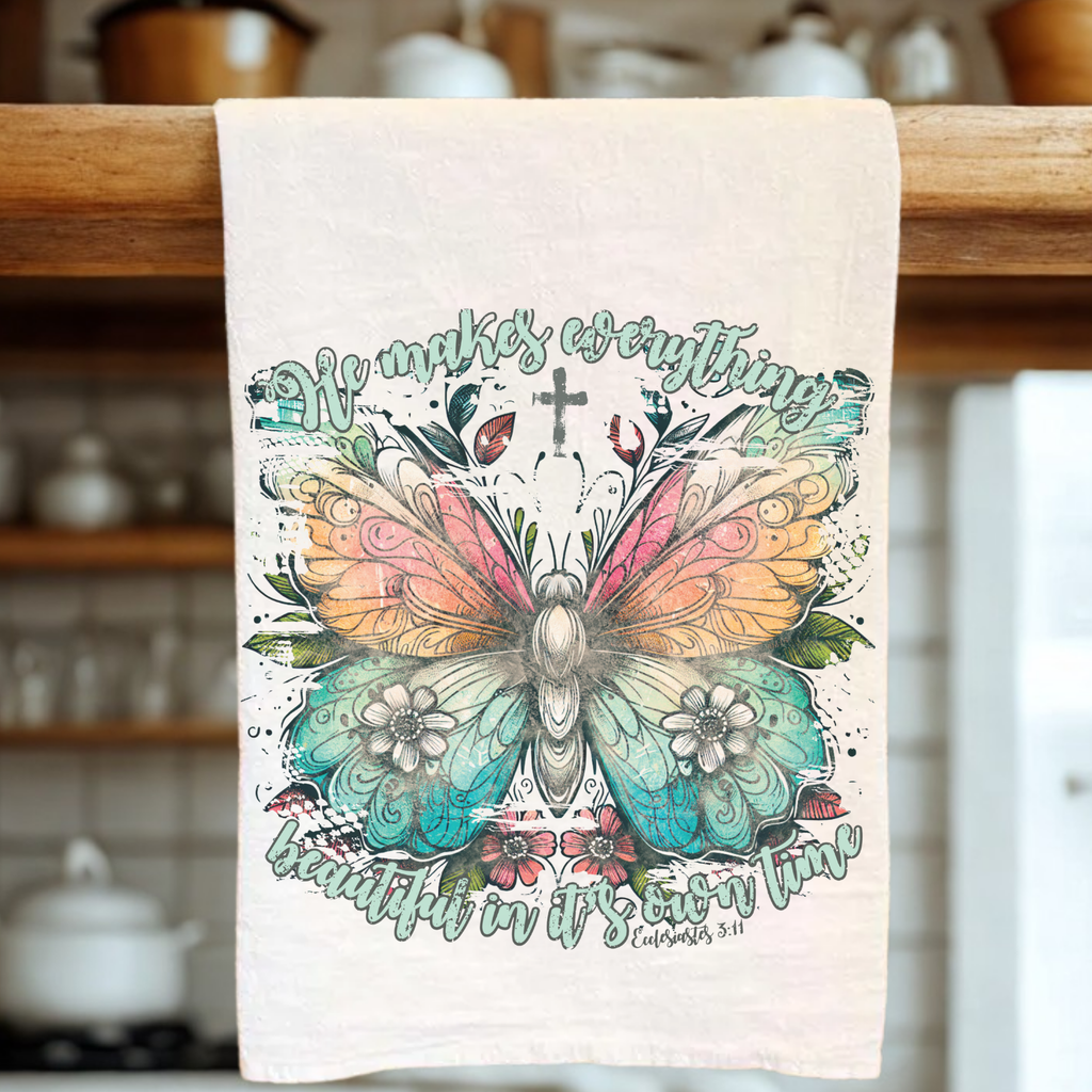 Decorative tea towel with butterfly design and text on a wooden rack in a kitchen.