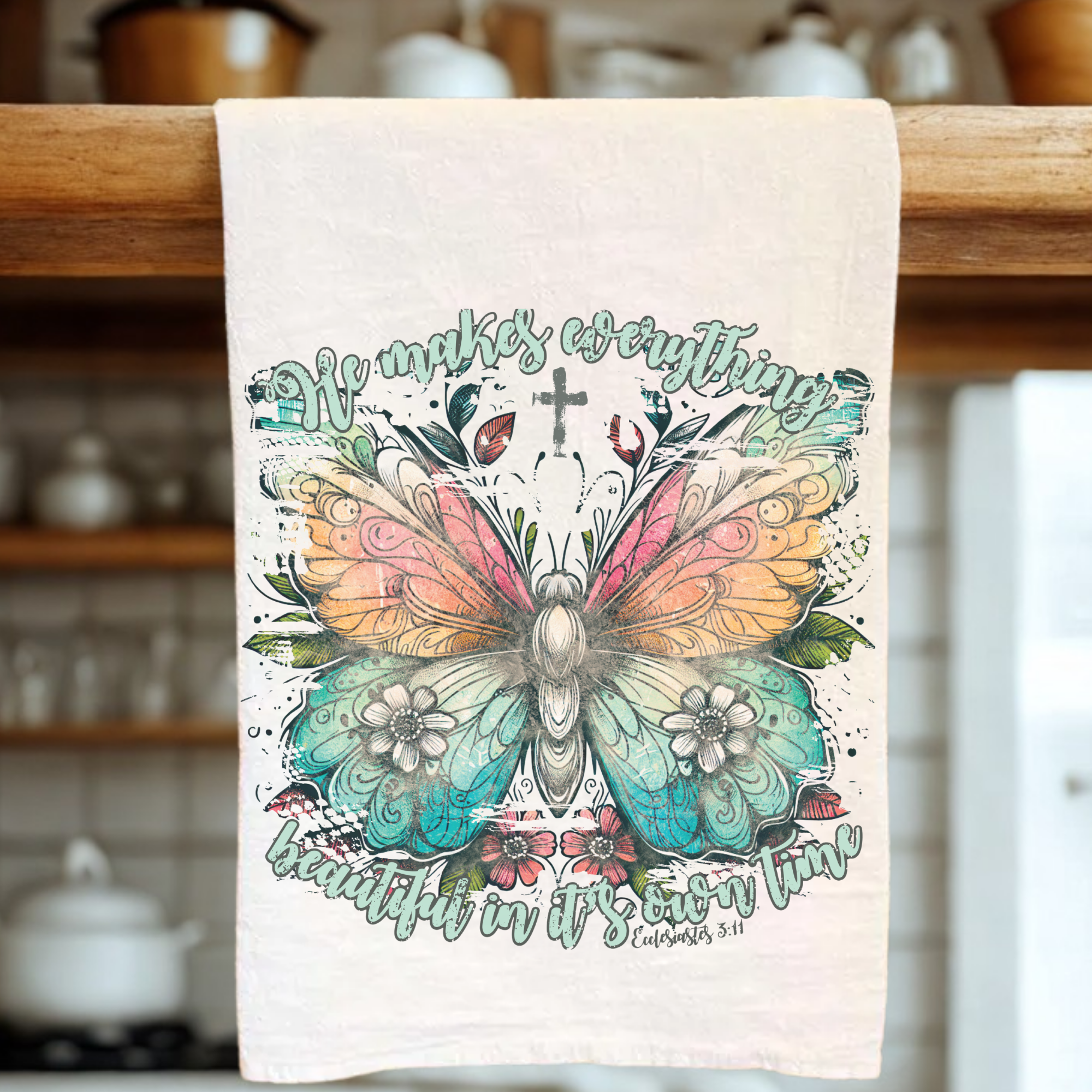 Decorative tea towel with butterfly design and text on a wooden rack in a kitchen.