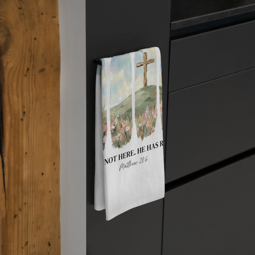 Decorative tea towel with religious design hanging on a black cabinet.