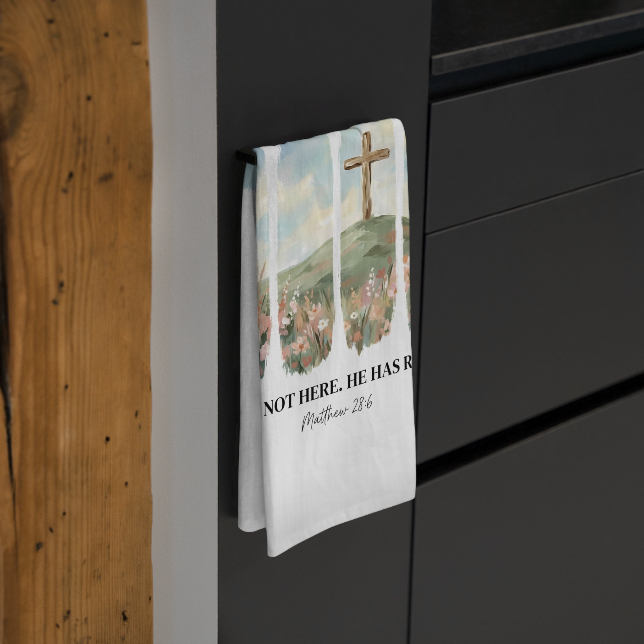 Decorative tea towel with religious design hanging on a black cabinet.