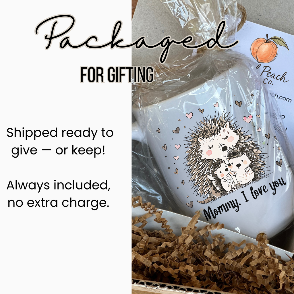White 15oz mug with hedgehog design and text 'Mommy, I love you' in a clear package tied with ribbon inside a white gift box filled with brown paper. 