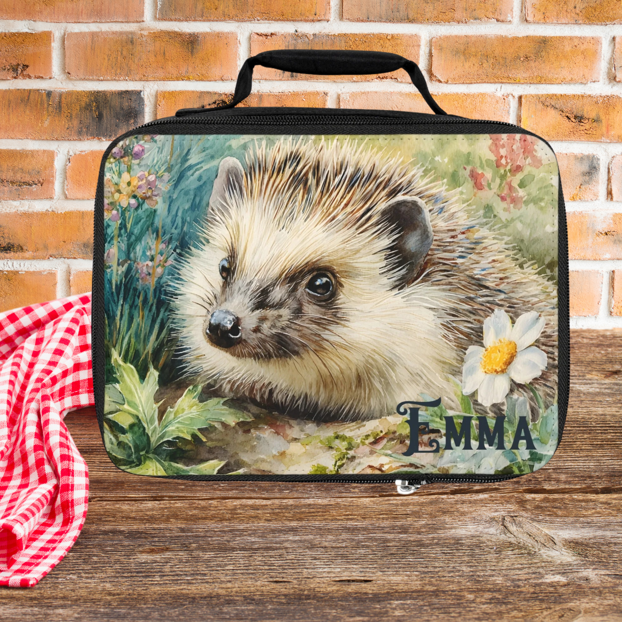 Lunch bag with hedgehog design and 'Emma' personalization on a wooden picnic table with brick background