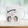 11 oz ceramic mug with a hedgehog couple design on a counter with a green background.