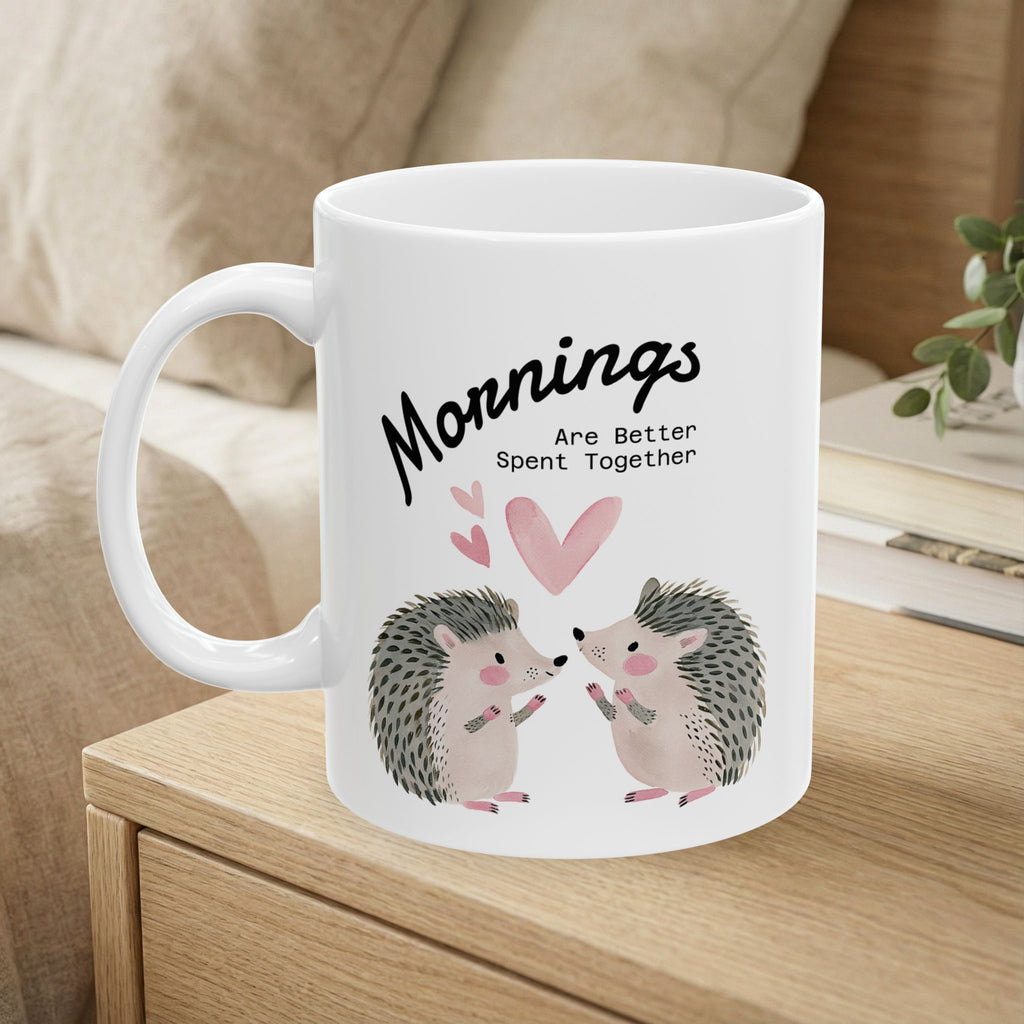 11 oz ceramic mug with a hedgehog couple design sitting on a bedside table 