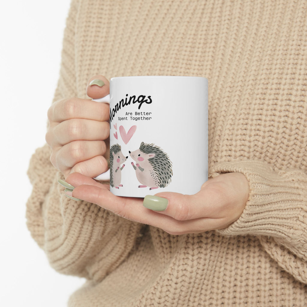 11 oz ceramic mug with a hedgehog couple design held by a person wearing a beige sweater.