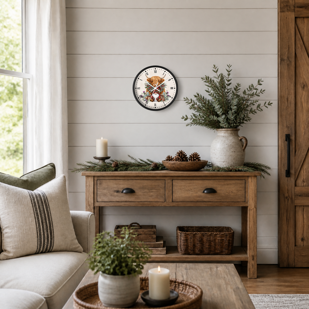A round wall clock featuring a festive gnome and highland cow illustration, styled in a cozy, rustic living room setting above a wooden console table with holiday greenery and candles.