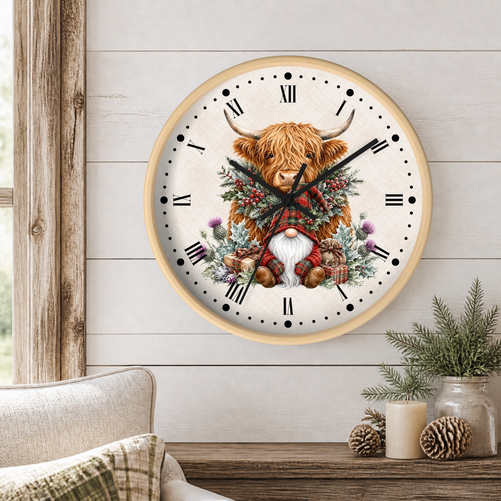 A round wall clock with a light wood frame hangs on a white shiplap wall above a rustic wooden table. The clock face features an illustration of a Highland cow wearing a red plaid kilt and a gnome in the center, surrounded by green foliage and purple thistles.