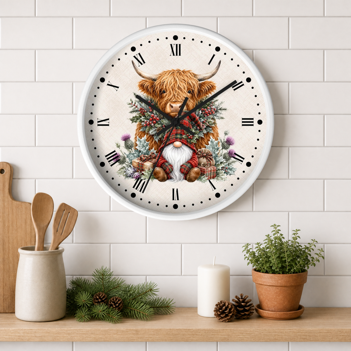 A round wall clock with a white face and black Roman numerals, featuring a festive illustration of a Highland cow with a red plaid scarf and a gnome at the center. The clock is mounted on a white subway tile wall above a wooden shelf styled with kitchen utensils, pine branches, a candle, and a potted plant.