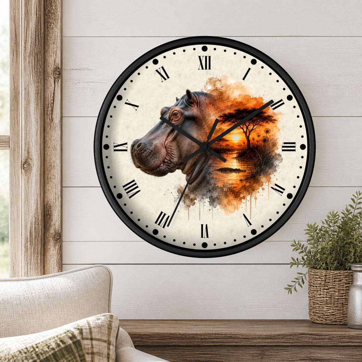 A round wall clock with a black frame and Roman numerals, featuring a hippopotamus illustration over an orange and brown watercolor landscape on the right side. The clock is mounted on a white shiplap wall above a wooden mantel with a small potted plant.