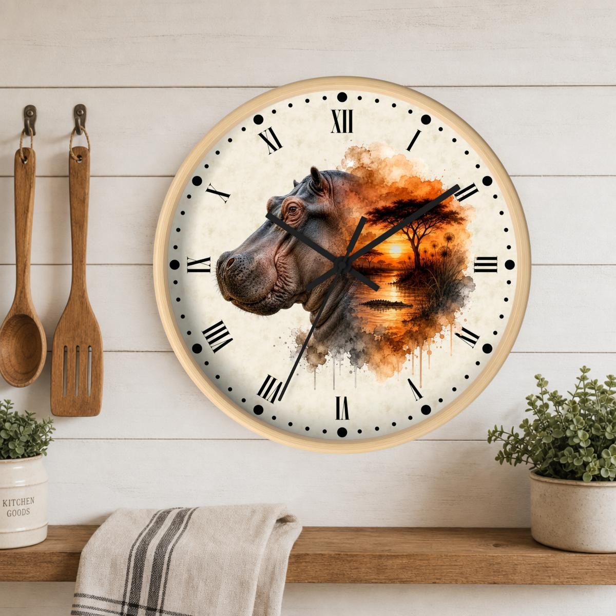 A round wall clock with a light wood frame hangs on a white wood-paneled wall above a shelf. The clock face features a watercolor-style hippopotamus illustration blending into an orange sunset scene.