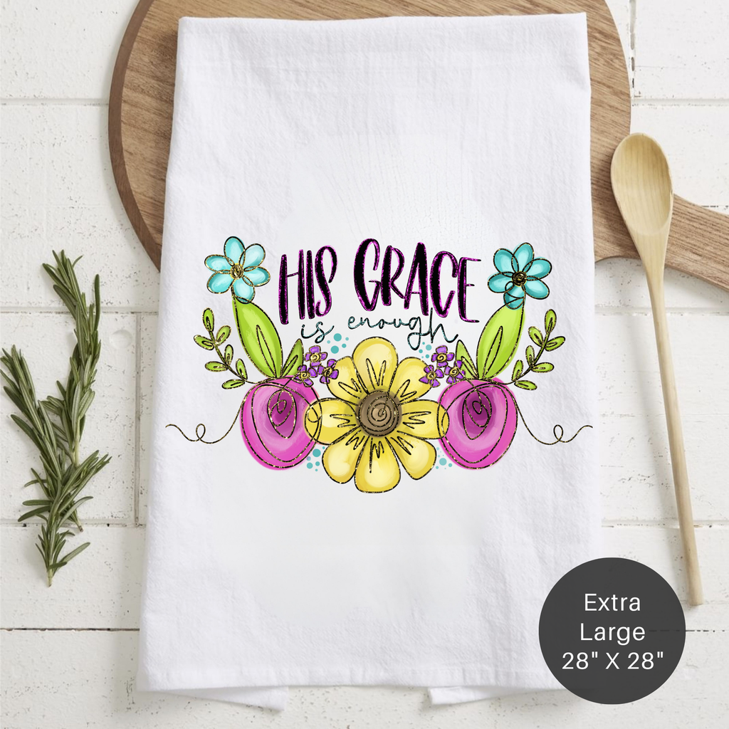 White tea towel with floral design and 'His Grace is Enough' text on a wooden surface.
