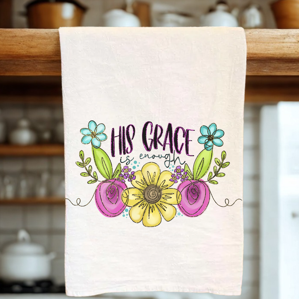 Decorative tea towel with floral design and 'His Grace is Enough' text hanging on a wooden rack.