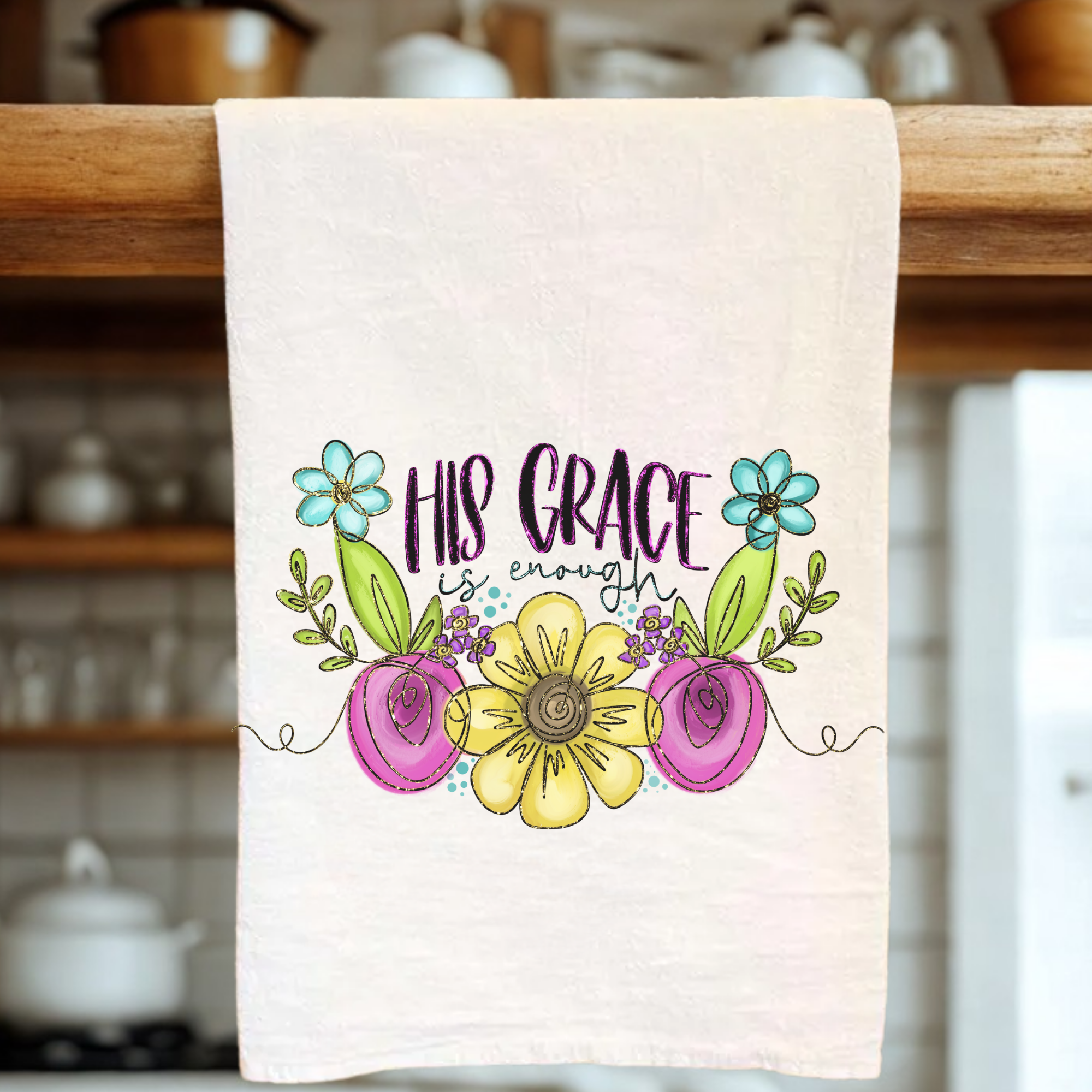 Decorative tea towel with floral design and 'His Grace is Enough' text hanging on a wooden rack.