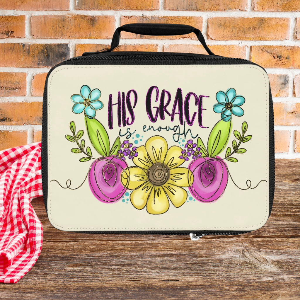 Lunch bag with floral design and 'His Grace is enough' text on a wooden picnic table against a brick wall background