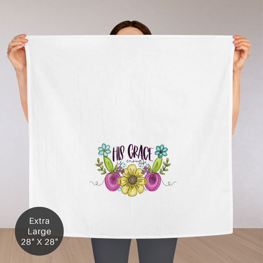Person holding an extra large white tea towel with floral design and text 'His Grace Is Enough'.