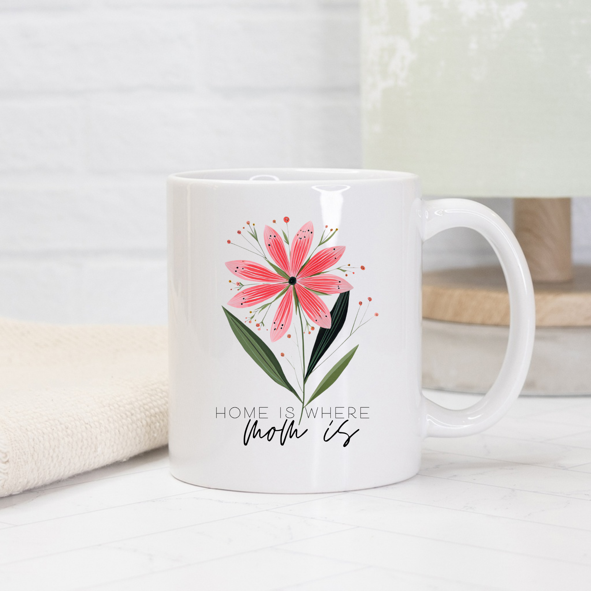White 11oz ceramic mug with a pink floral design and text 'Home is where mom is' on a light background 