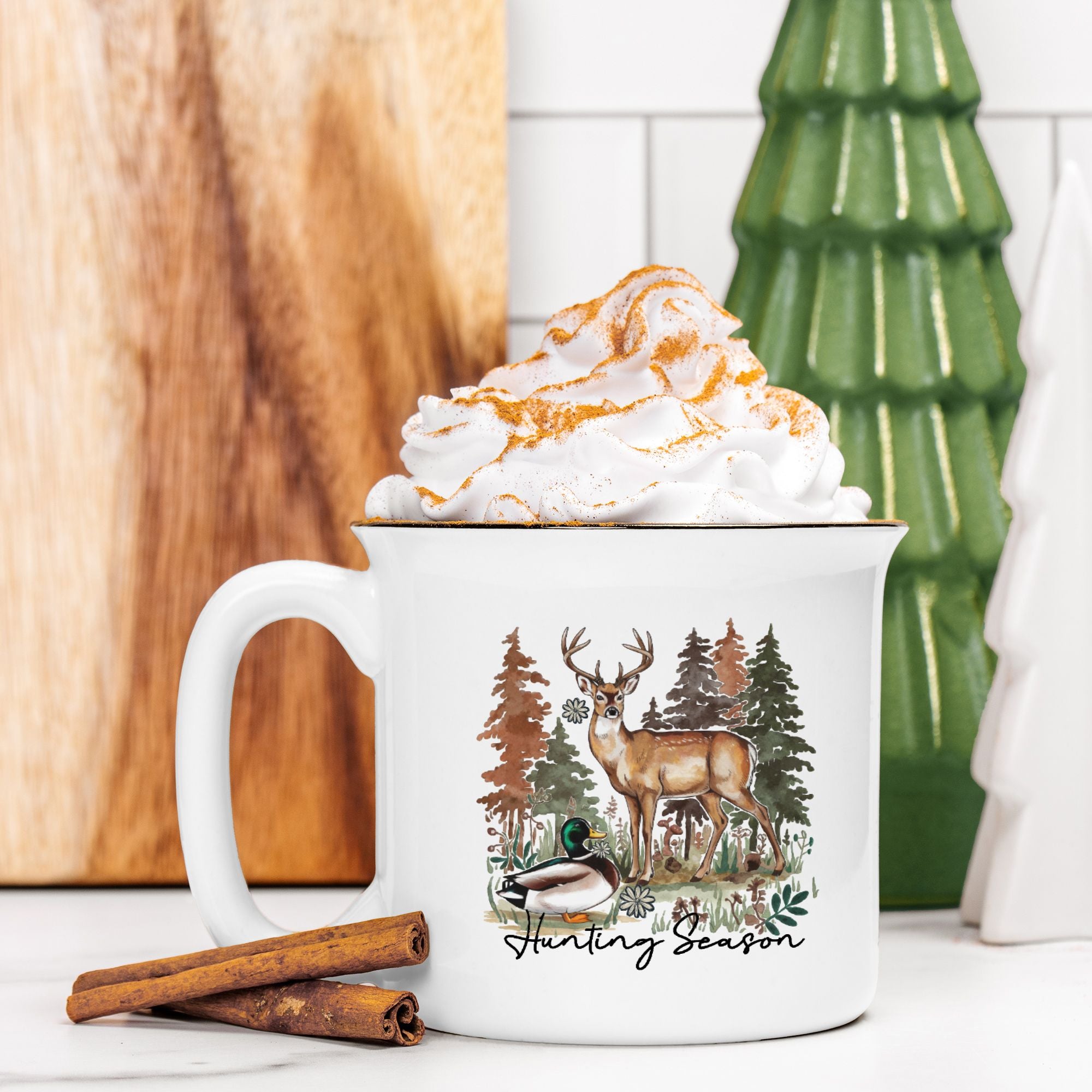 Mug with 'Hunting Season' design featuring a deer and trees, filled with hot chocolate and whipped cream.