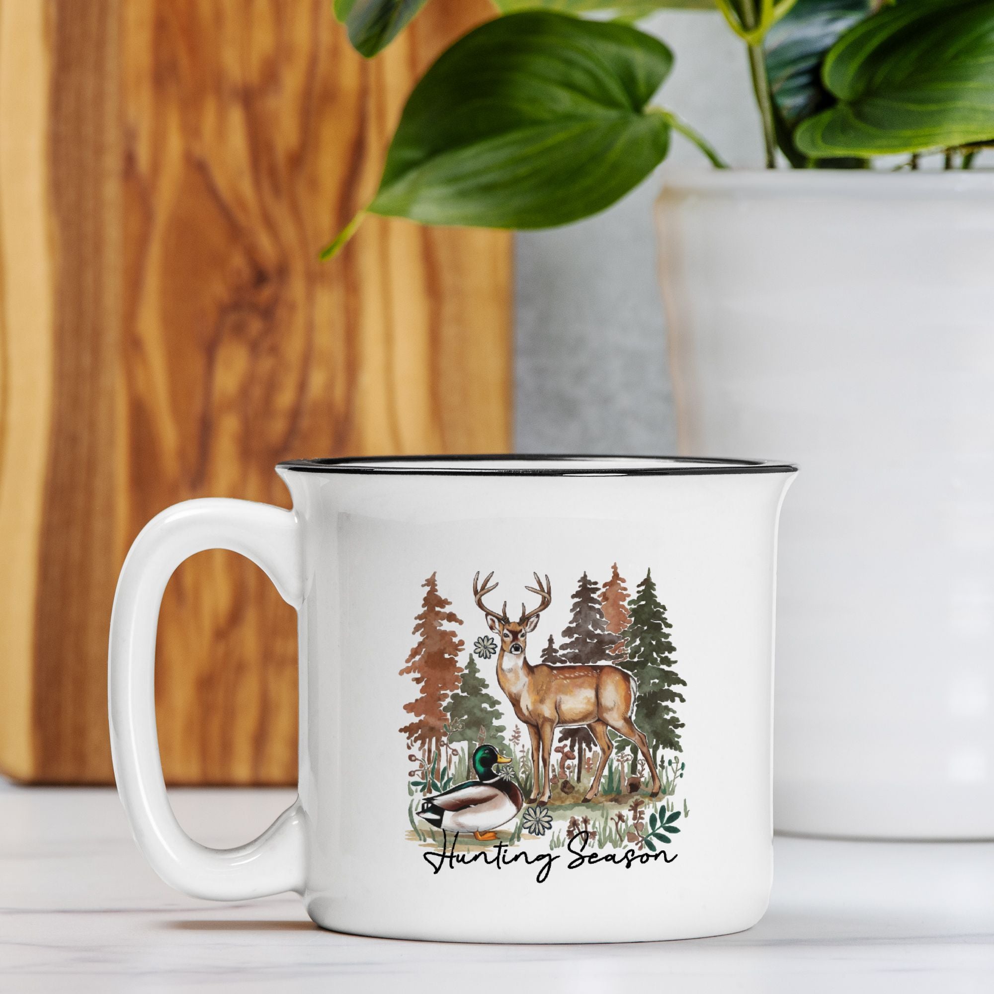 White mug with nature-themed design featuring a deer and trees on a wooden surface.