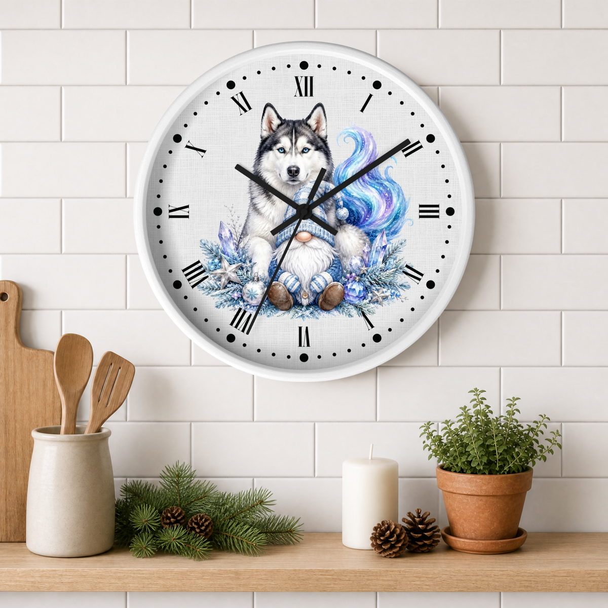 A round wall clock with a white face and black Roman numerals, featuring an illustration of a husky dog surrounded by blue flowers and a colorful blue-purple mane. The clock is mounted on a white subway tile wall above a wooden shelf styled with kitchen utensils, pine branches, a candle, and a potted plant.
