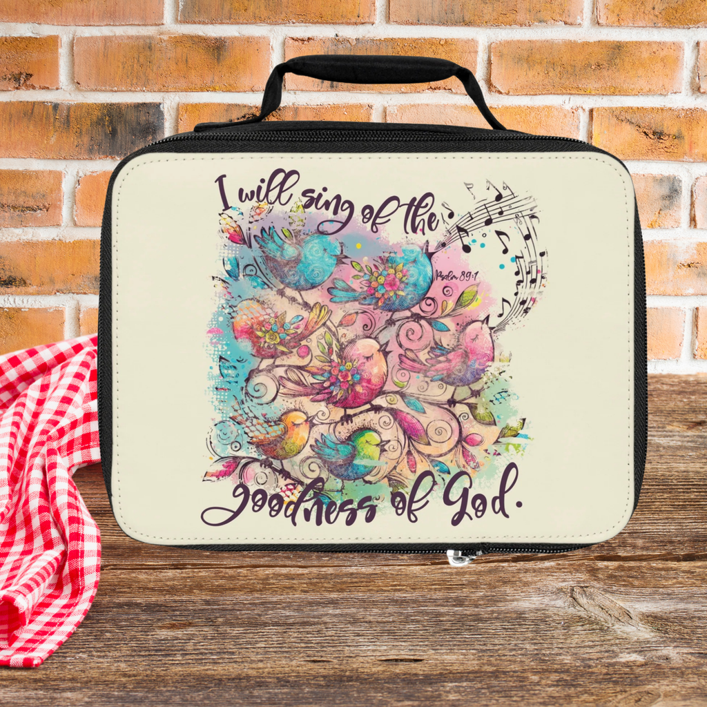 insulated lunch bag with colorful design and text 'I will sing of the praises of God' on a wooden picnic table with brick background