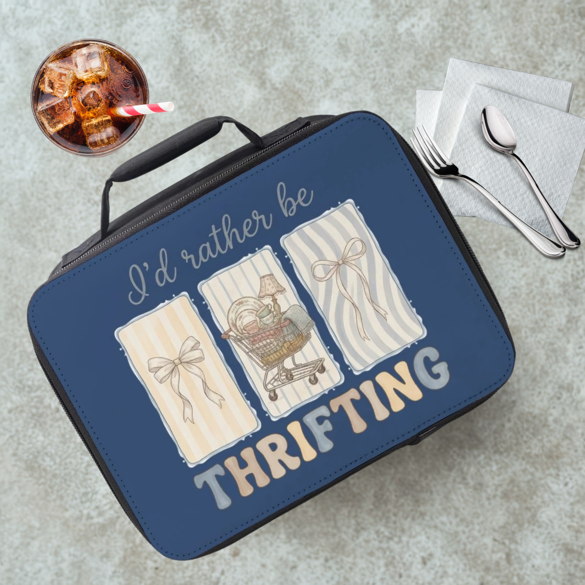 Black and blue lunch bag with 'I'd rather be thrifting' text and illustrations on a cafeteria table with a drink and utensils.