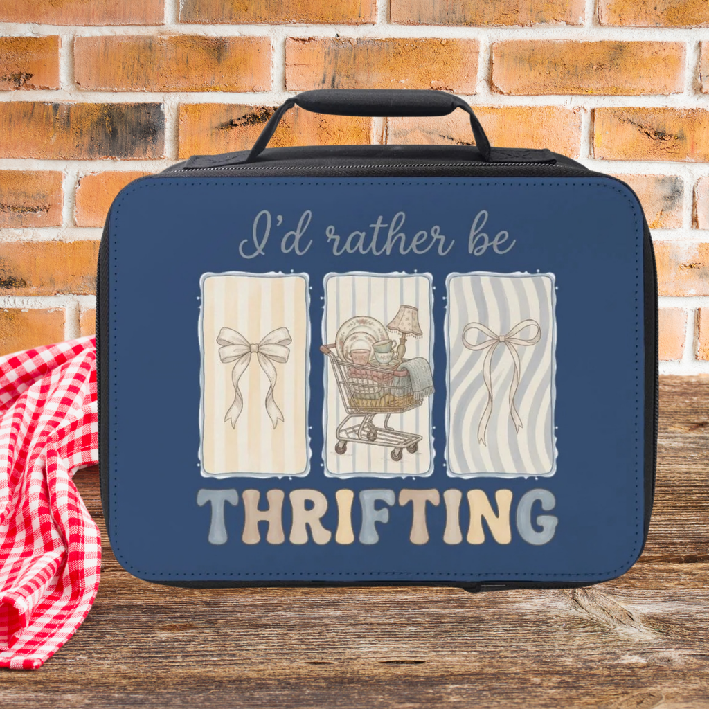 Blue lunch bag with 'I'd rather be thrifting' text and illustrations on a picnic table against a brick wall background