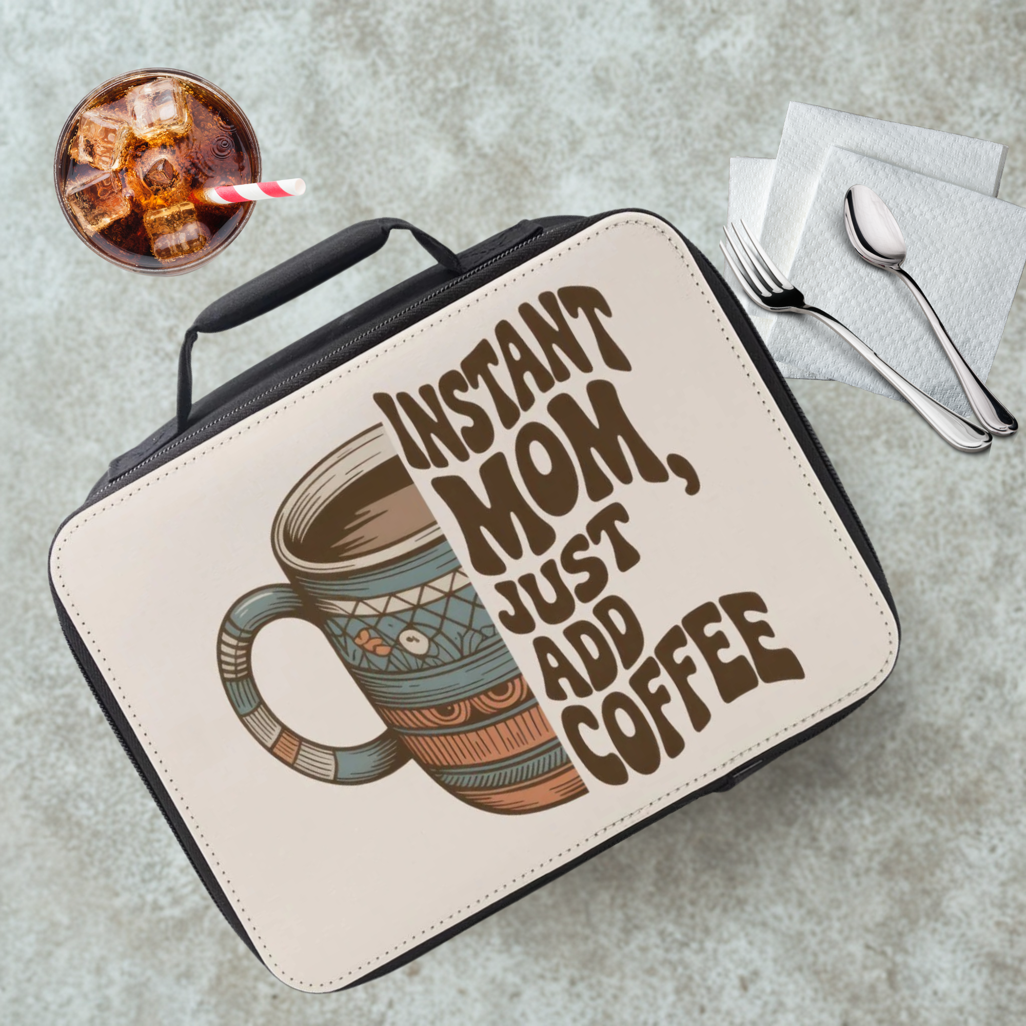 Lunch bag with 'Instant Mom, Just Add Coffee' text and coffee graphic on a cafeteria table with a drink and utensils.
