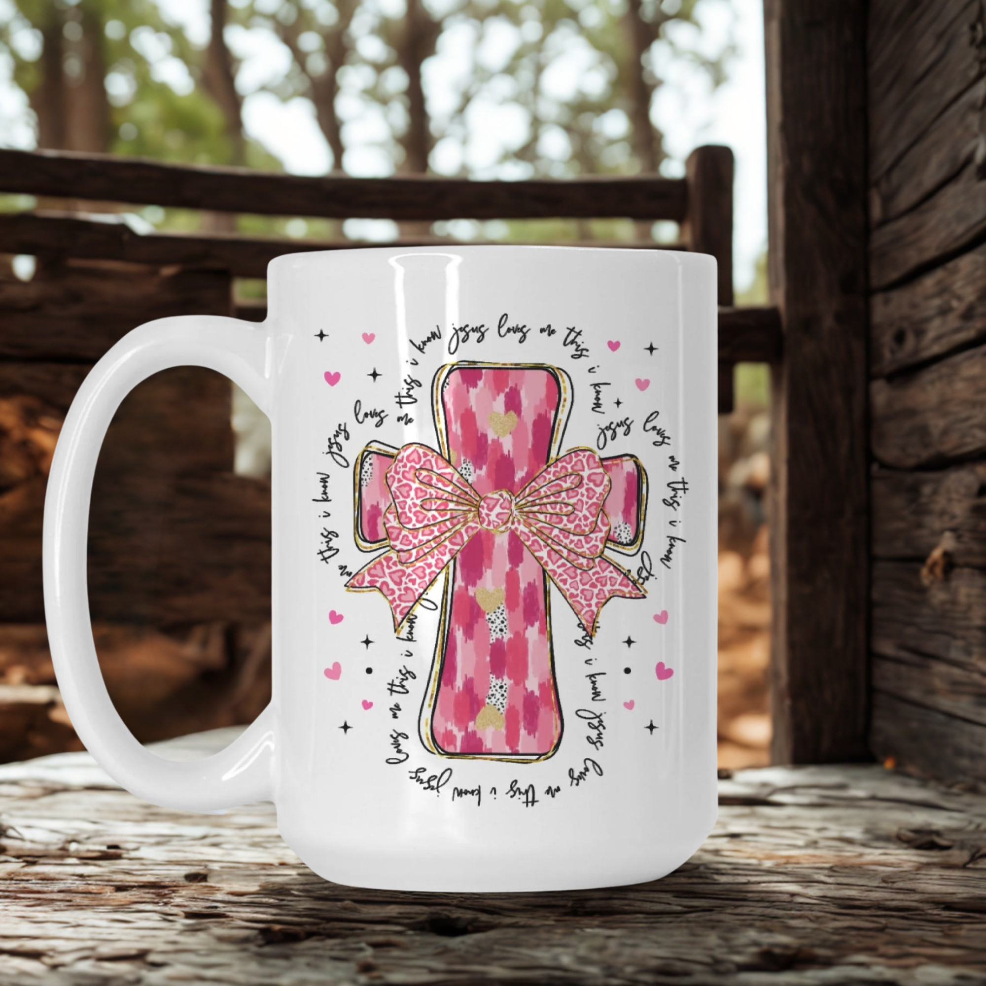 White mug with pink cross and bow design on a wooden surface