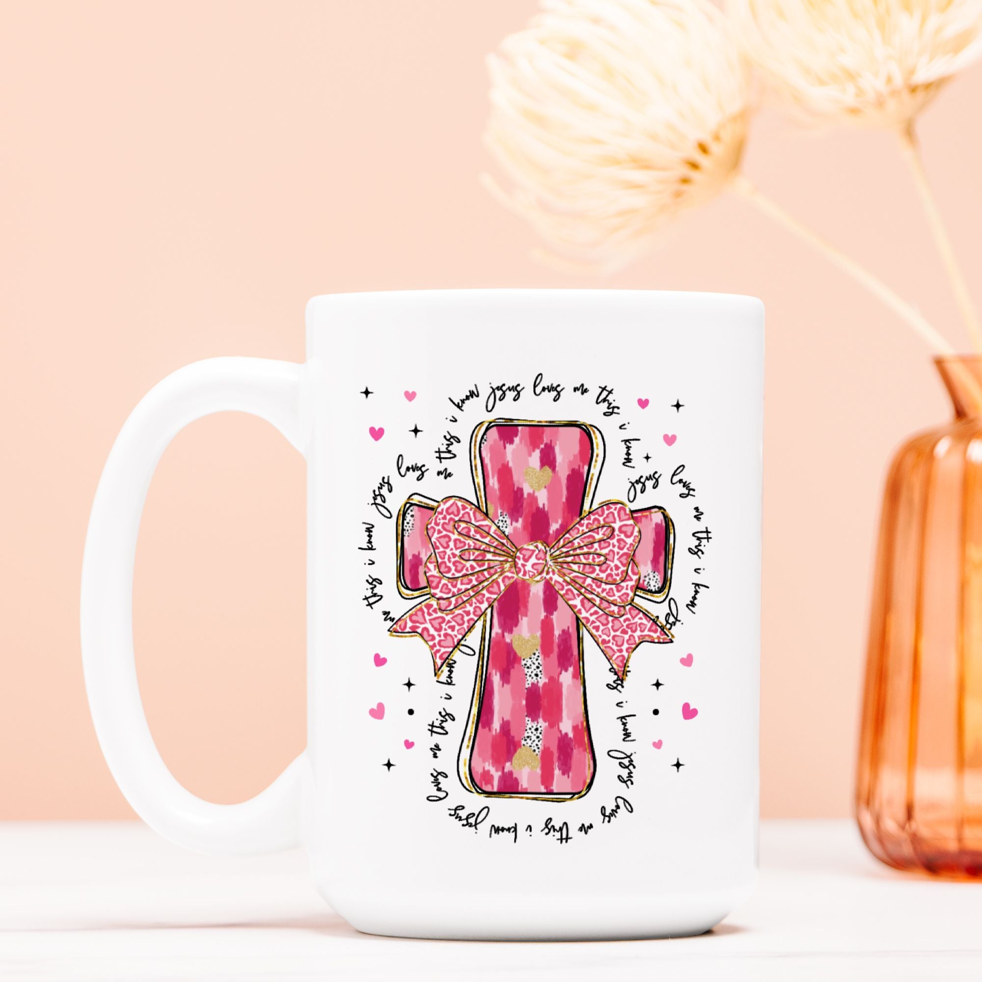 White mug with pink cross and bow design on a light pink background