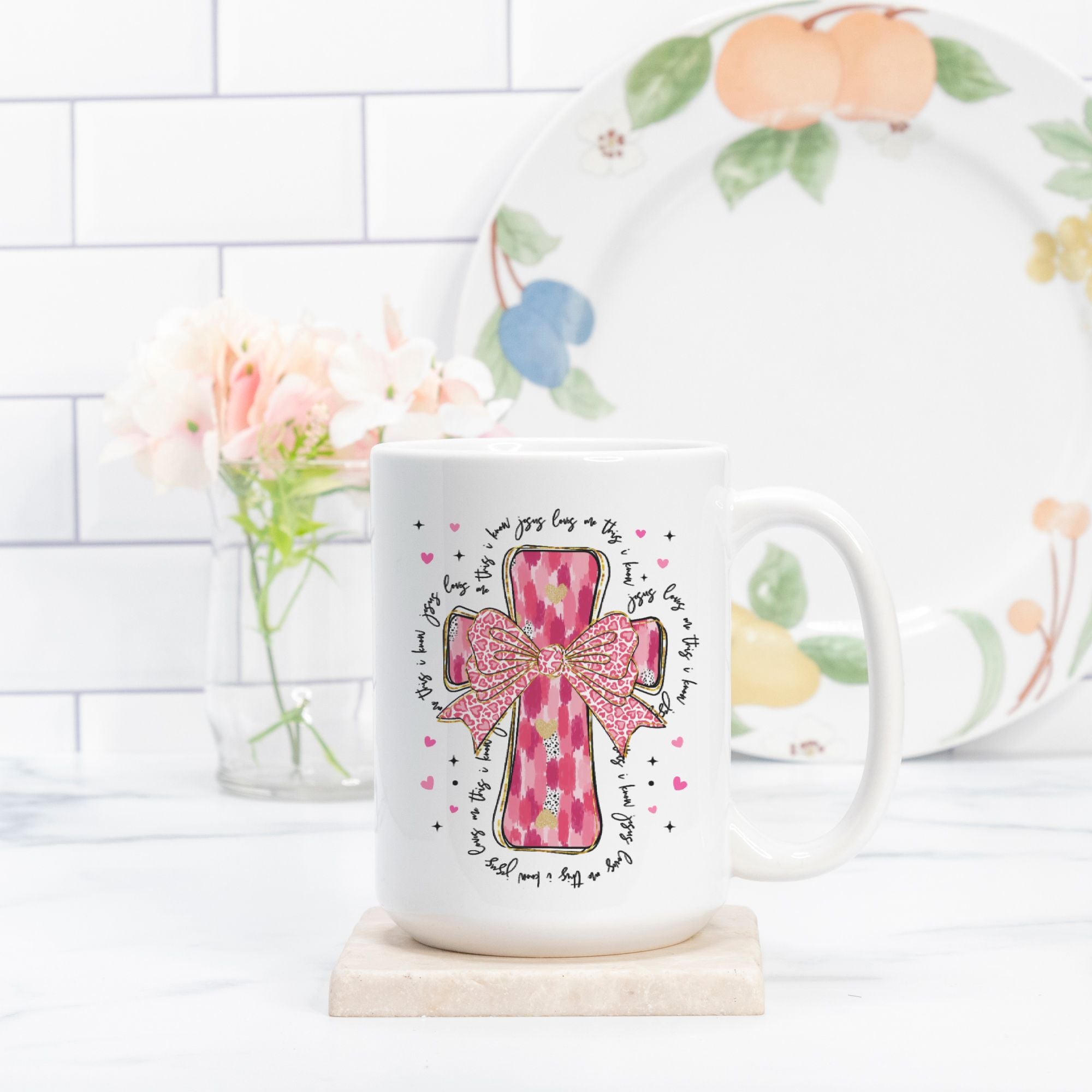 White mug with pink cross design on a white surface with a floral plate in the background.