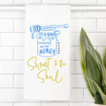 Decorative tea towel with honey jar and text on a white tiled wall.