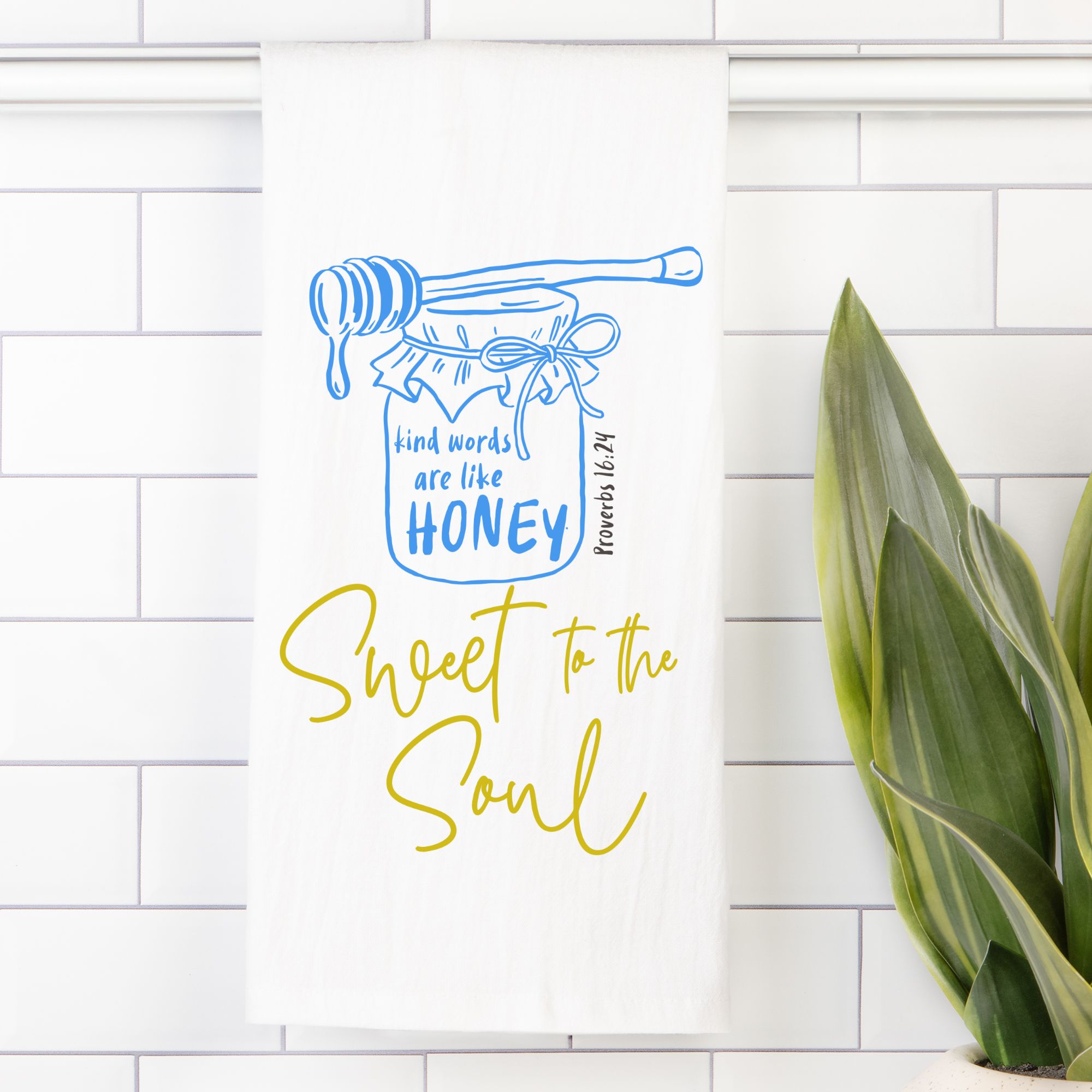 Decorative tea towel with honey jar and text on a white tiled wall.