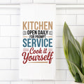 Colorful text on a white tea towel with a plant to the right.